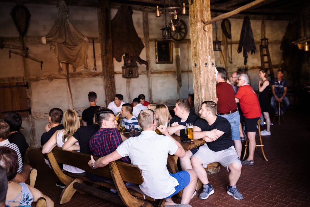 Menschen sitzen und stehen in einer rustikalen Gaststätte und unterhalten sich.