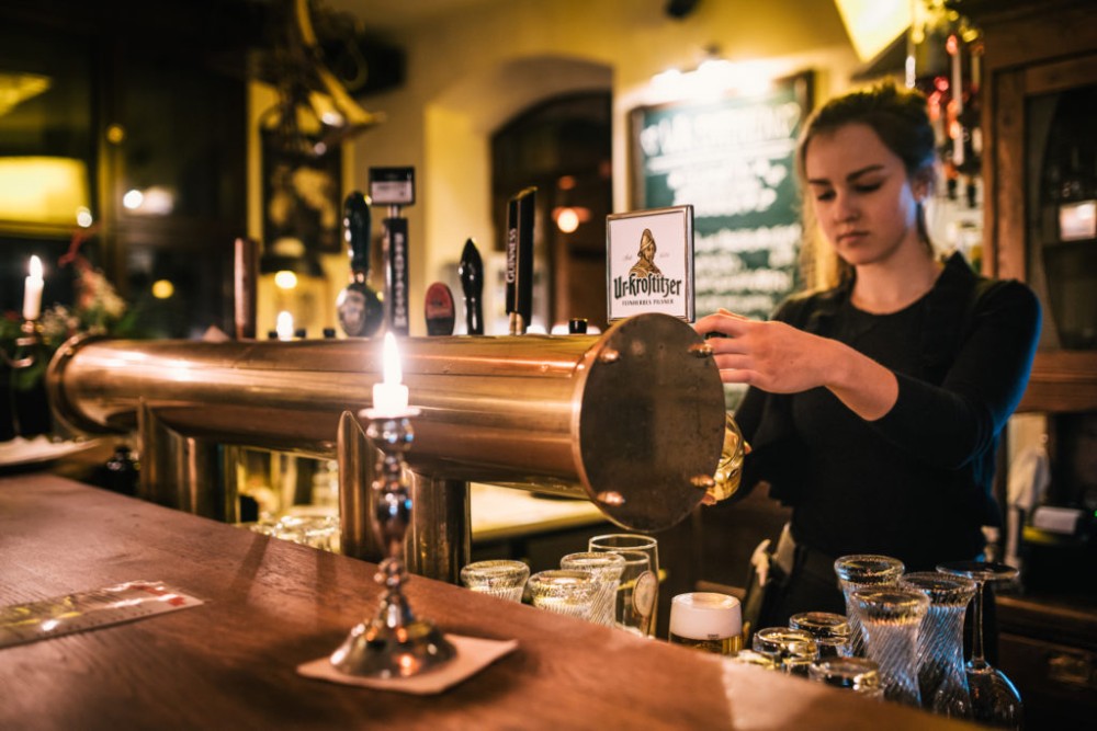 Eine junge Frau bedient am Bartresen, reinigt ein Bierglas mit einem Tuch.