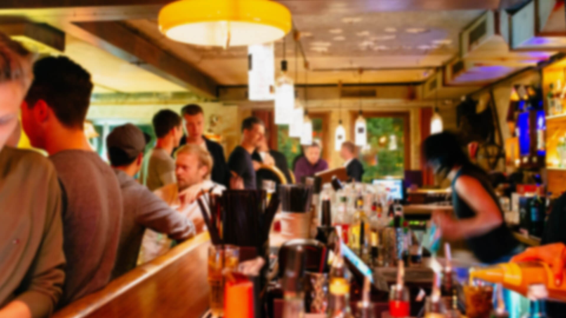 Menschen stehen an einer belebten Bar, während ein Barkeeper Getränke zubereitet.