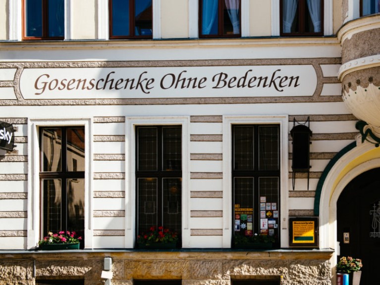 Fassade eines historischen Gebäudes mit Beschriftung und Blumen vor den Fenstern.