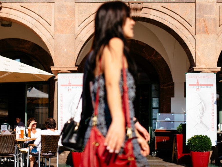 Eine unscharfe Frau geht an einem Café mit Gästen im Hintergrund vorbei.