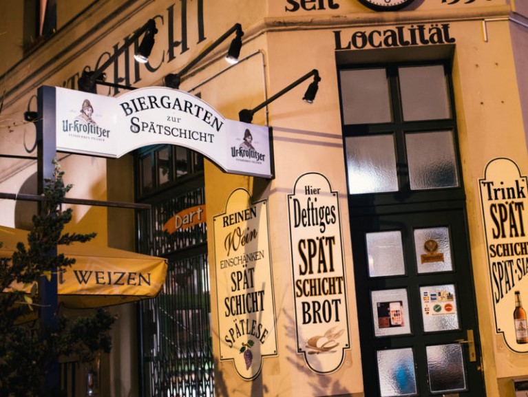 Eingang eines Lokals bei Nacht mit beleuchteten Schildern und Biergartenaufschrift.