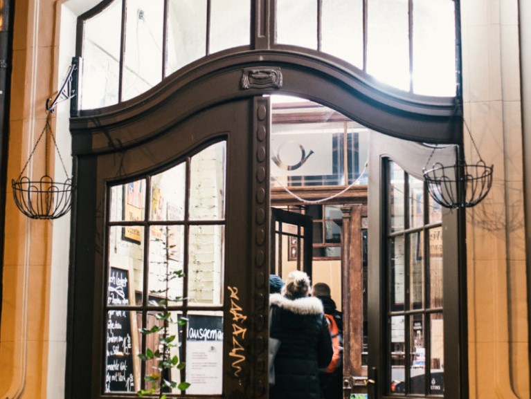 Drei Personen stehen vor dem Eingang eines eleganten Gebäudes.