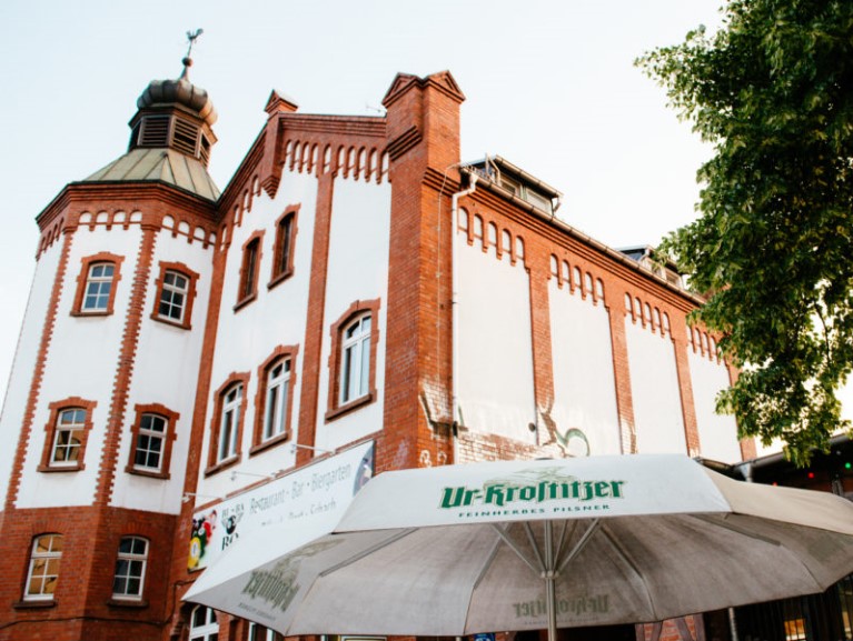 Eine gotische Backsteinfassade ragt hinter einem großen Sonnenschirm empor. Der Himmel ist klar.