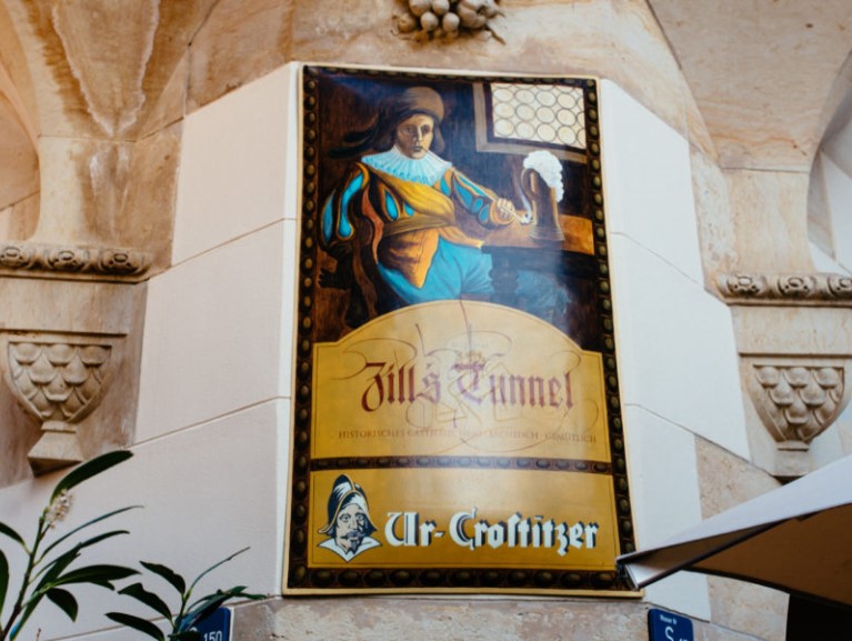 Gemaltes Schild zeigt eine Frau in mittelalterlicher Kleidung, die eine Laute spielt.