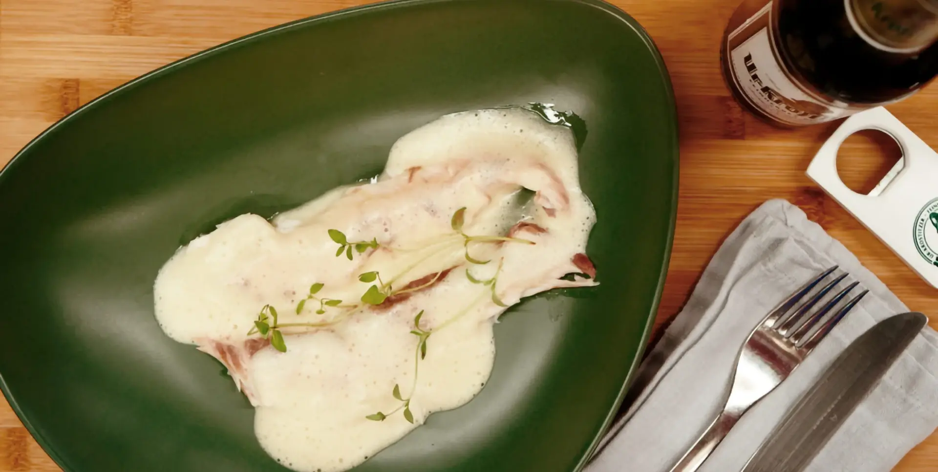 Ein grüner Teller mit Dorade und heller Soße, garniert mit Kräutern, liegt neben Besteck.