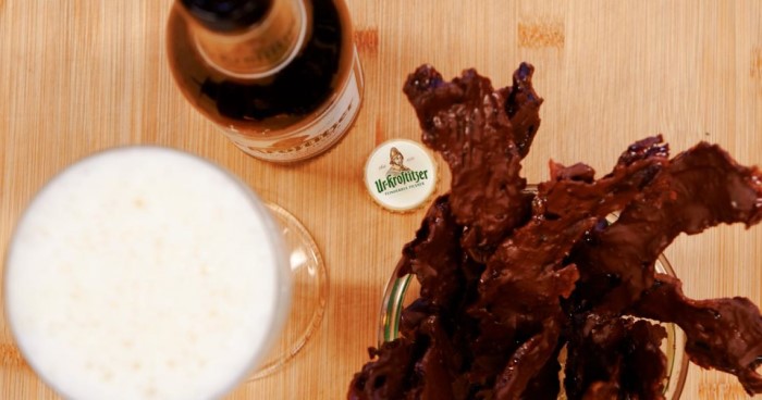 Ein Glas helles Bier steht neben einer Flasche und Baconchips.