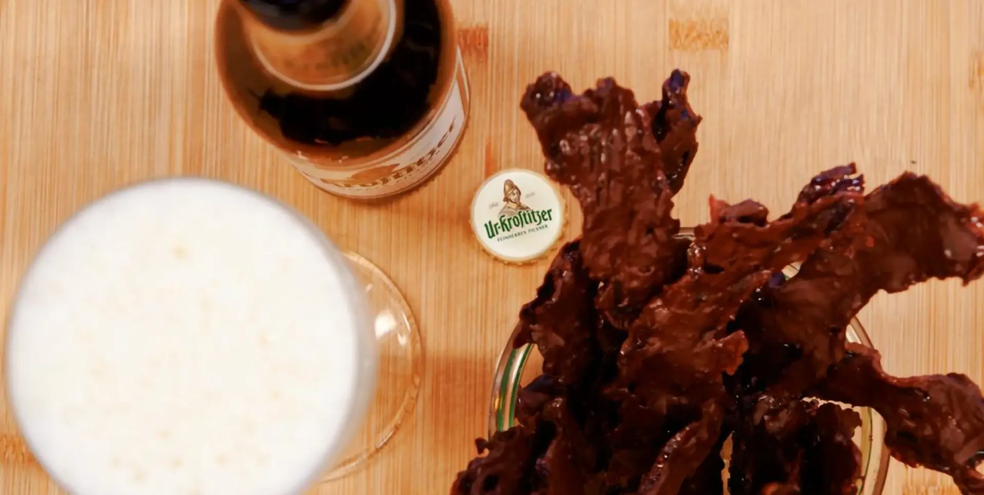 Ein Glas helles Bier steht neben einer Flasche und Baconchips.