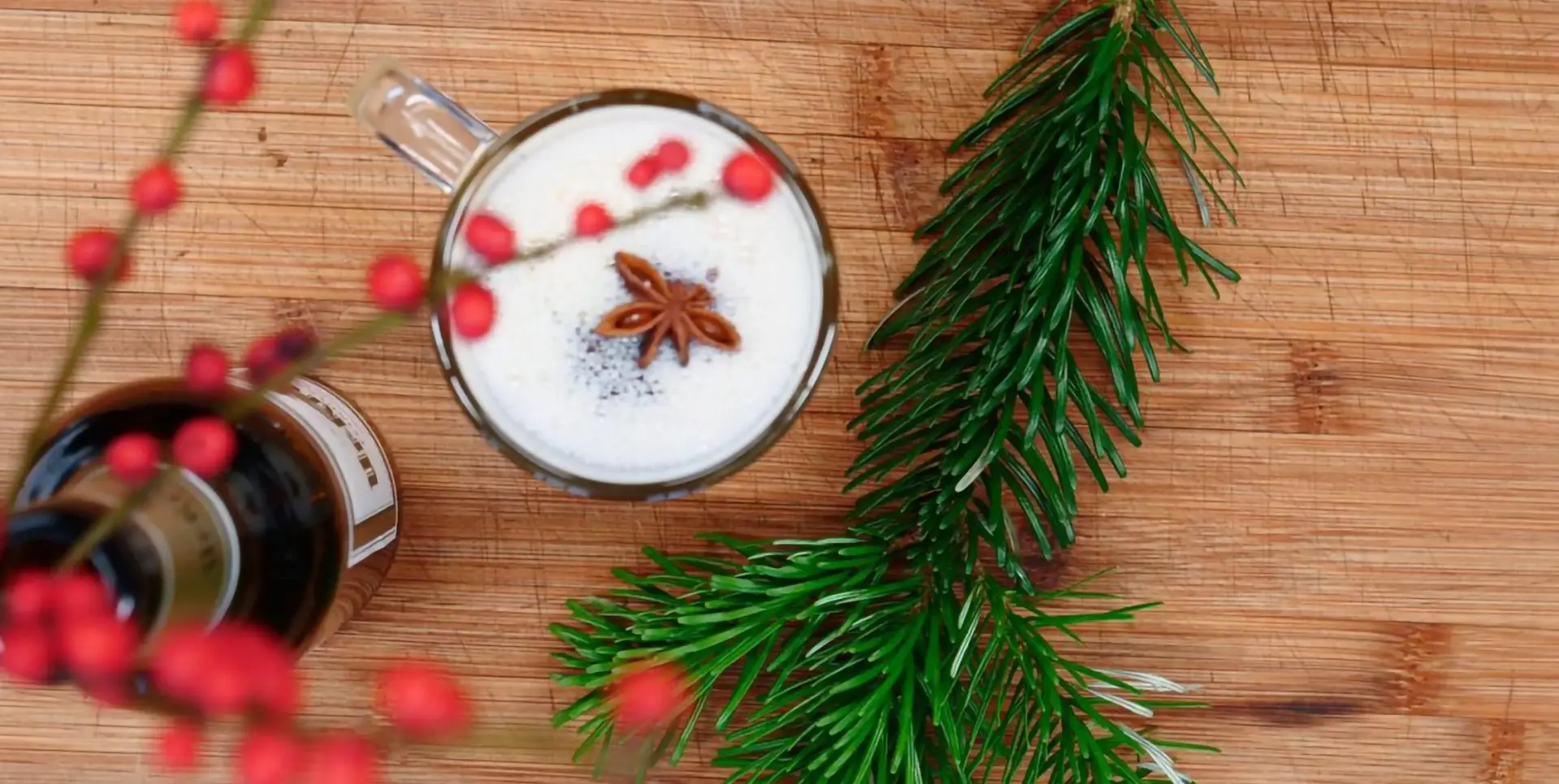 Ein weihnachtlicher Drink mit Beeren und Sternanis garniert liegt neben Tannenzweigen auf einem Holztisch.