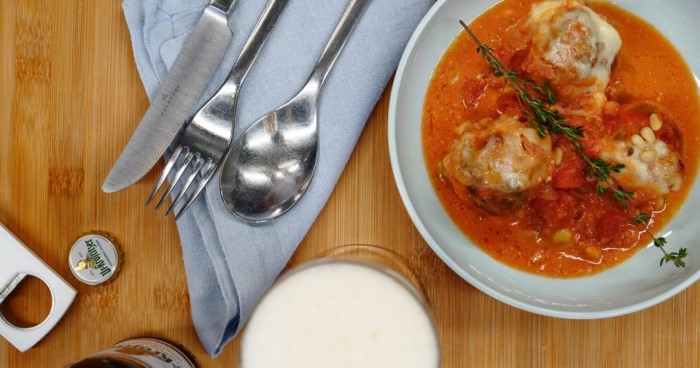 Ein Teller mit Fleischbällchen in Tomatensauce auf einem Holztisch neben Besteck.