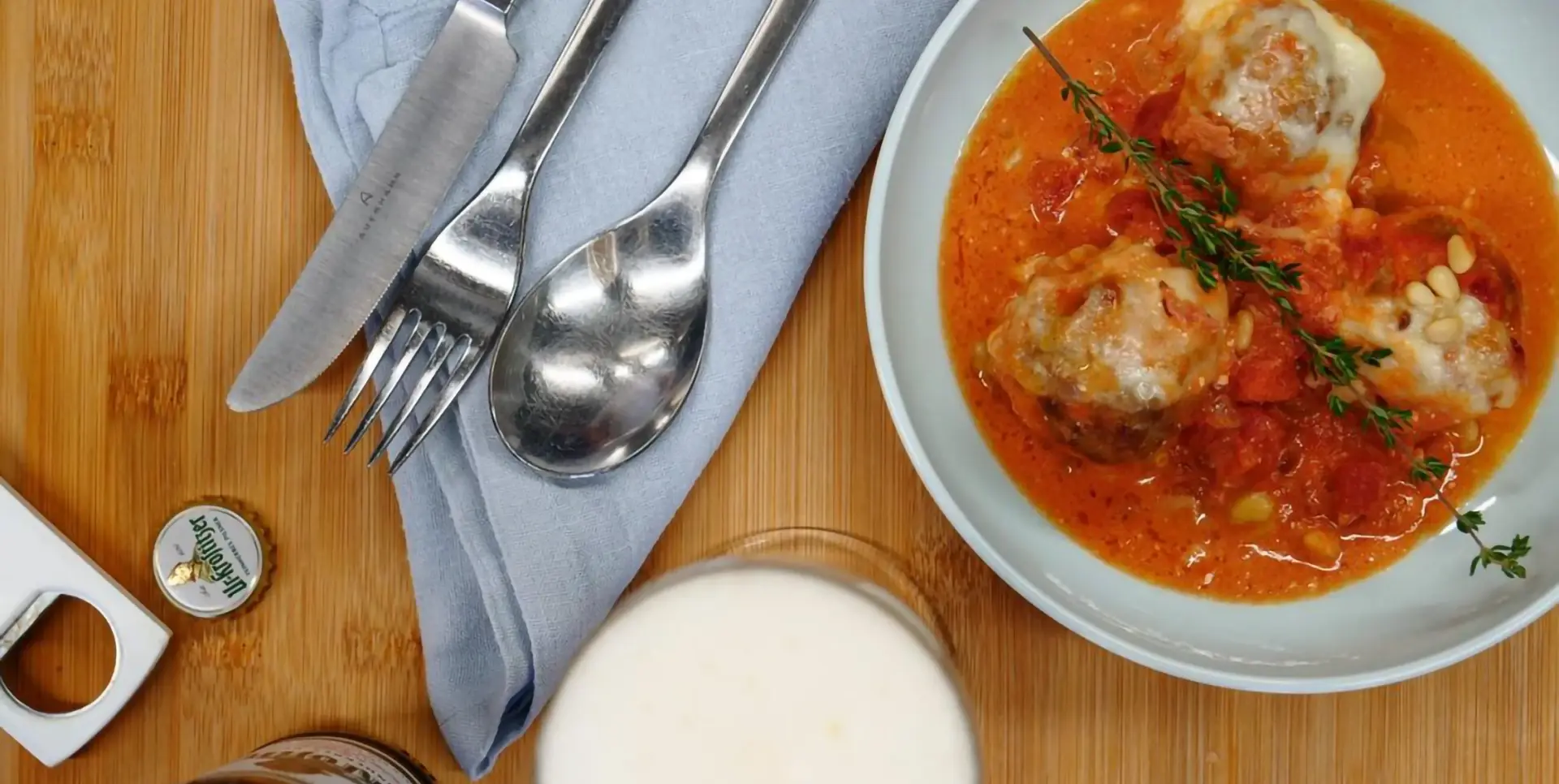 Ein Teller mit Fleischbällchen in Tomatensauce auf einem Holztisch neben Besteck.