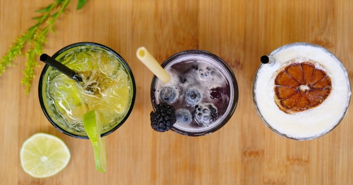 Drei verschiedene Cocktails stehen auf einem Holztisch, von oben betrachtet.