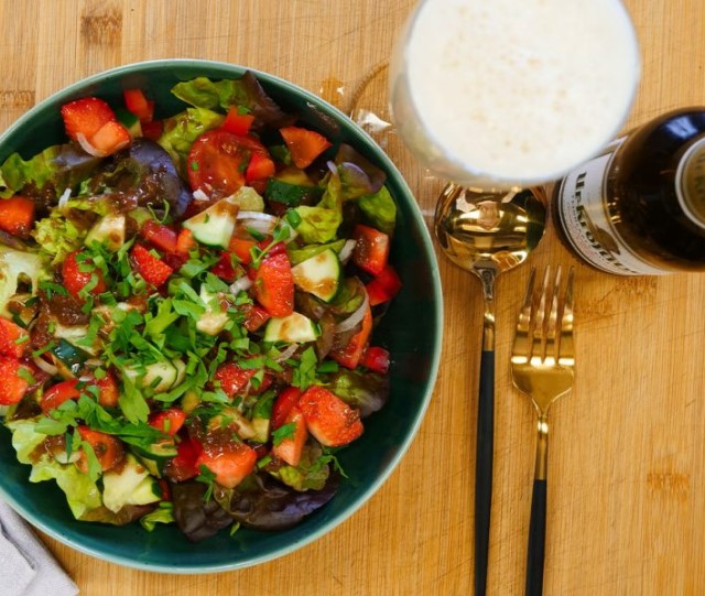 Ein frischer Salat mit Erdbeeren und Gemüse steht neben einem Glas Bier auf einem Holztisch.