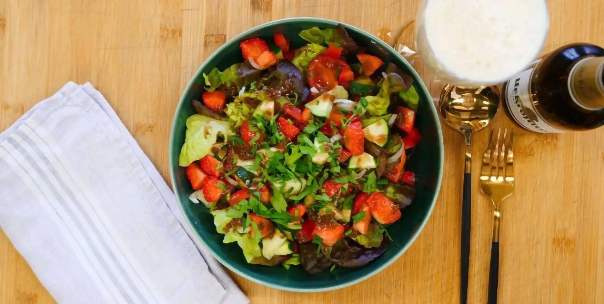 Ein bunter Salat mit Erdbeeren und Gemüse in einer grünen Schüssel auf einem Holztisch.