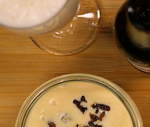 Eine Schale mit cremiger Suppe und dunklen Einlagen steht auf einem Holztisch. Daneben sind ein Glas und eine Flasche zu sehen.