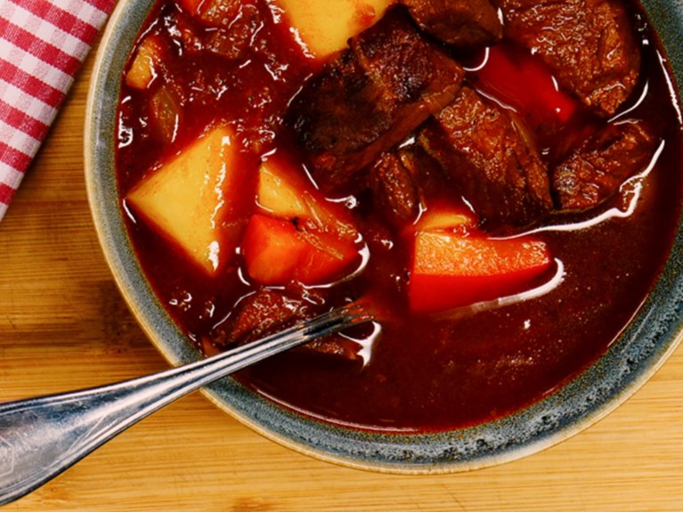Ein Teller mit Rindfleisch und Kartoffeln in dunkler Soße, serviert auf einem Holztisch.