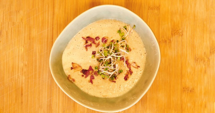 Eine Schüssel mit cremiger Suppe, garniert mit Speck und Sprossen.