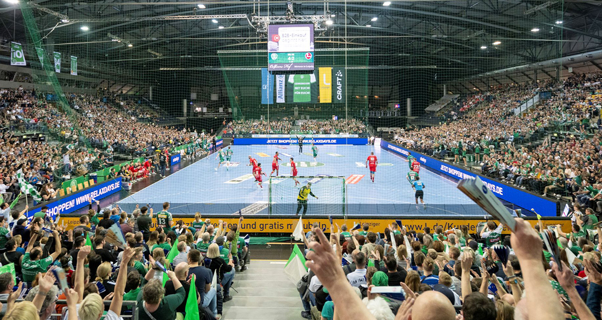 Ein Handballspiel in einer Großsporthalle, in der Mitte das Spielfeld, drumherum jubelnde Zuschauer.