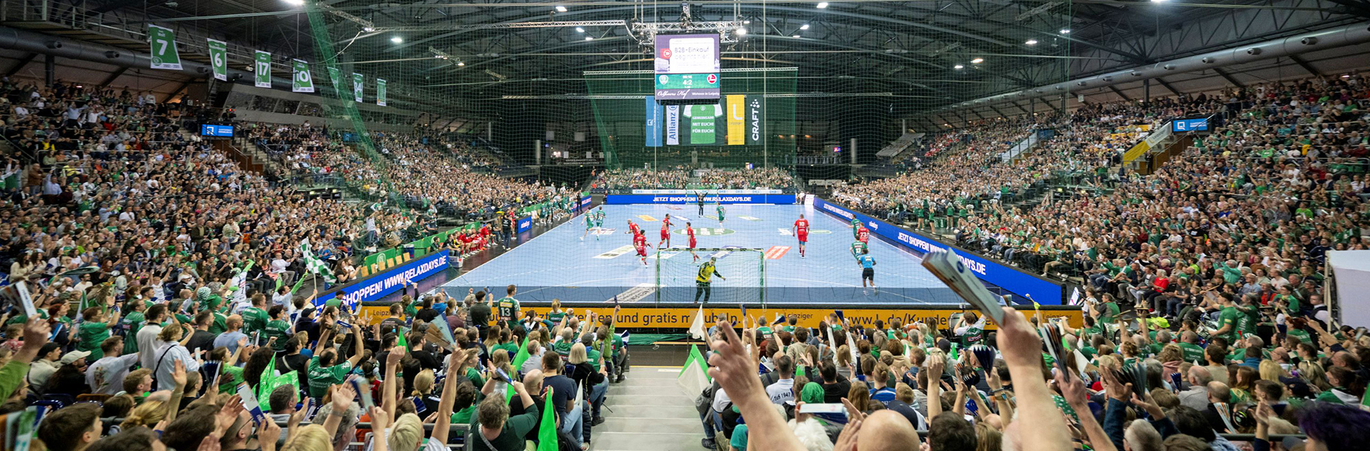 Ein Handballspiel in einer Großsporthalle, in der Mitte das Spielfeld, drumherum jubelnde Zuschauer.